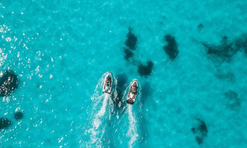 Aerial view of two jet skis on clear blue ocean water creating white trails